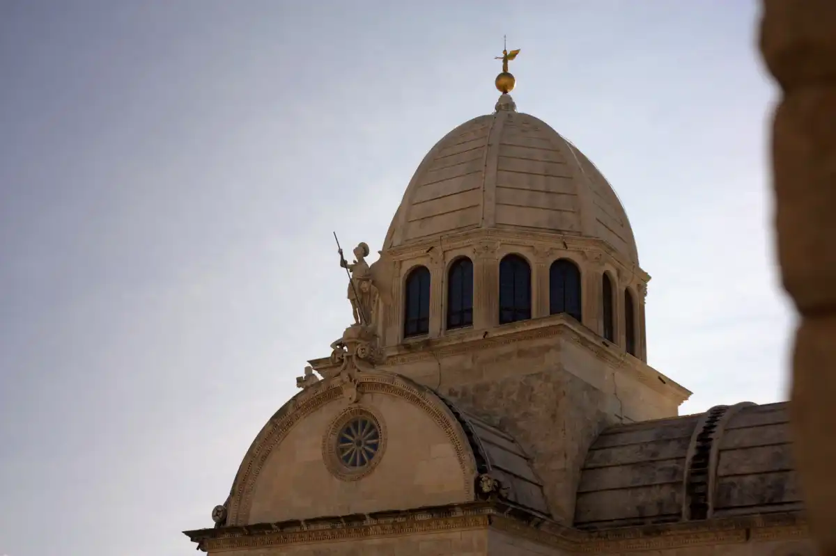 Exterior dome of Šibenik Cathedral with saint statue under clear skies