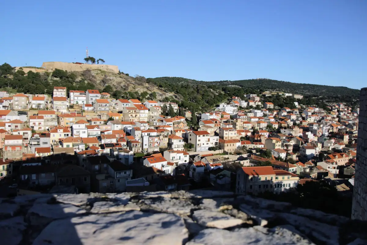 Dense rooftops of Šibenik's old town leading up to the fortresses on the hill, captured from the perspective of another fortress.