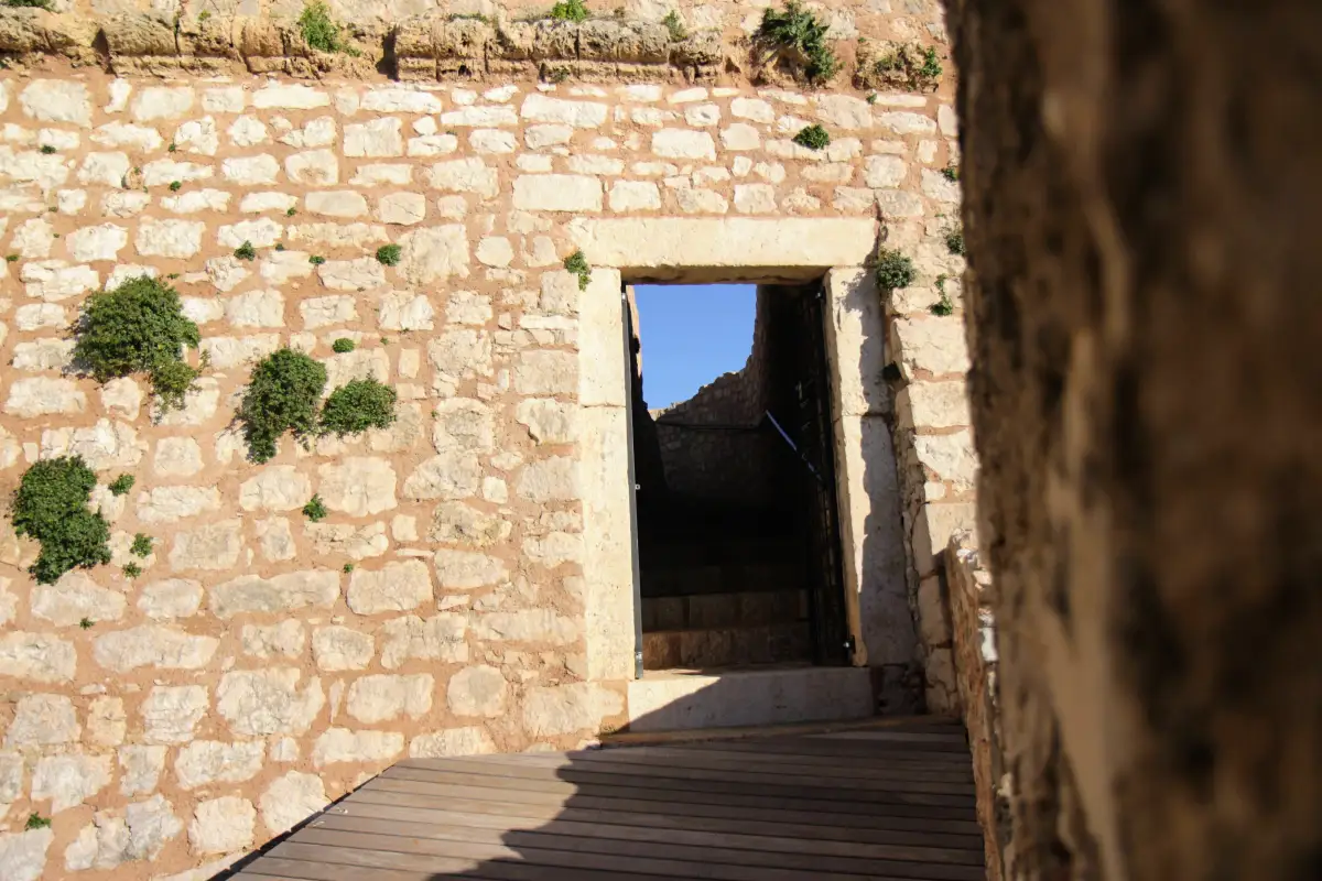 Stone doorway leading to the interior of St. John's Fortress in Šibenik, with wooden decking and tufts of greenery emerging from the walls.
