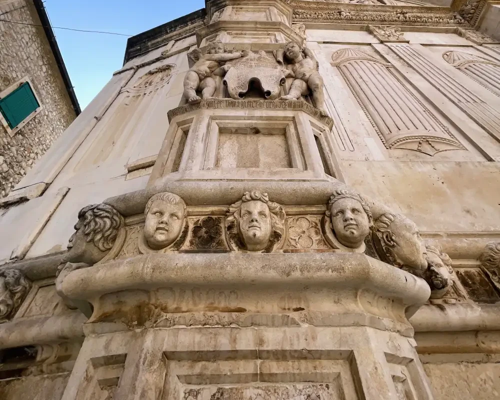 The image shows a detailed close-up of the ornate stonework at St. James Cathedral in Šibenik, Croatia