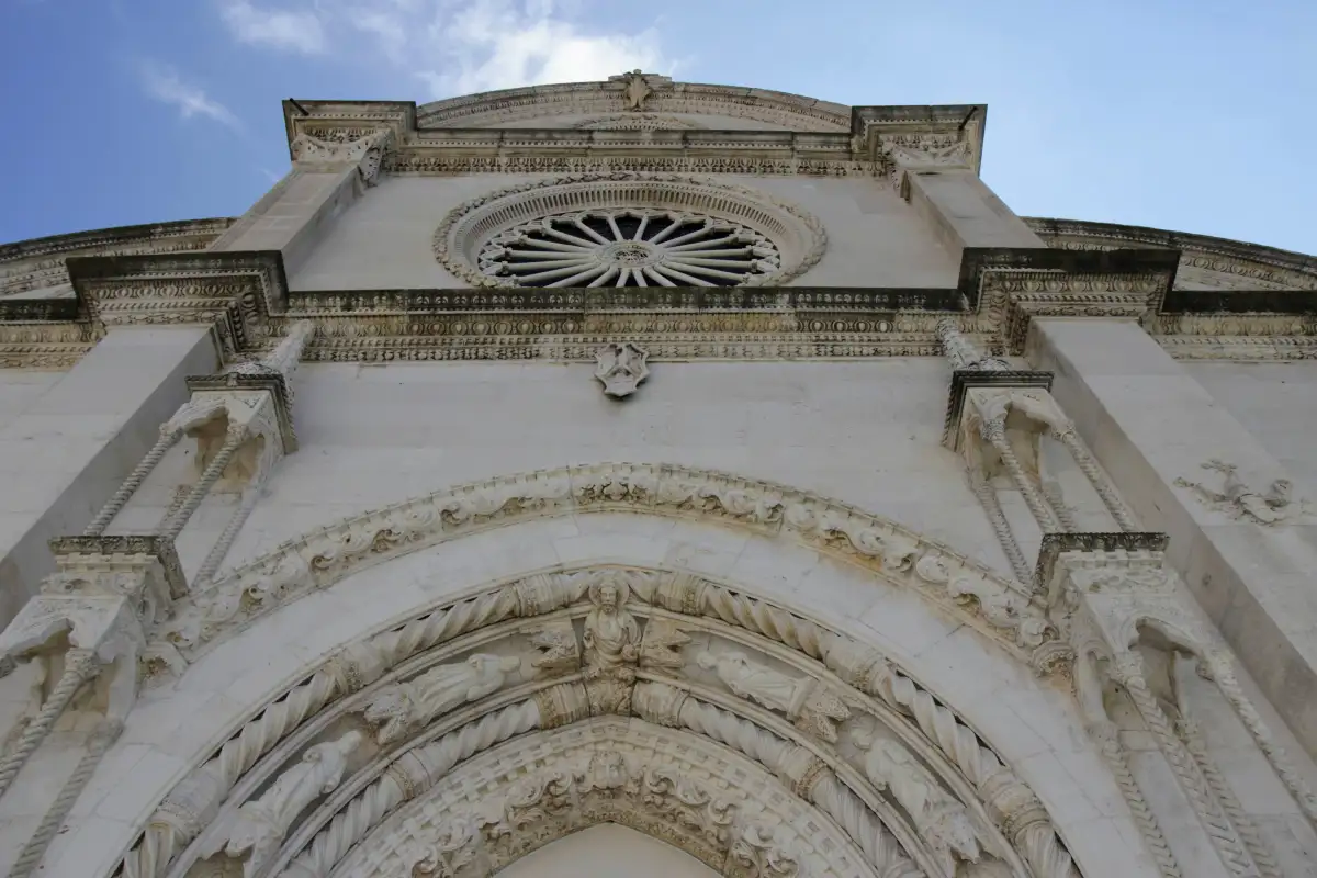 Ornate façade of Šibenik's Cathedral of St. James, with a detailed rose window and Gothic architecture, viewed from below.