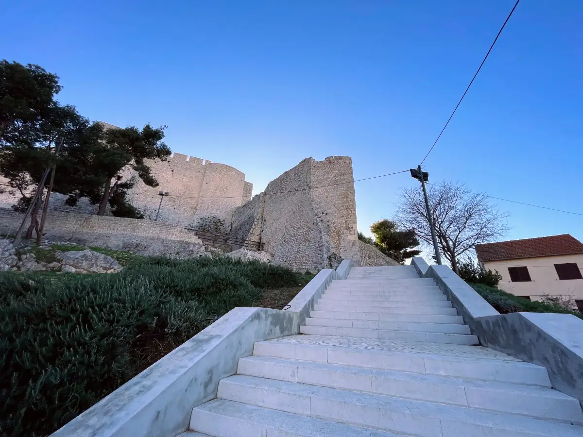 White staircase leading up to the ancient walls of St. Michael's Fortress in Šibenik during twilight.
