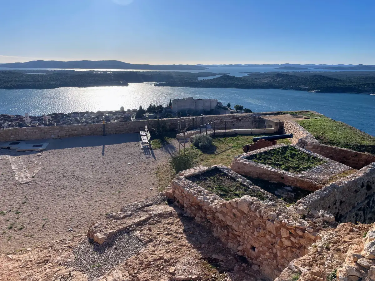 alt="Overlooking the sunlit expanse of the Adriatic Sea from the ruins atop St. John's Fortress in Šibenik, with the old town in the foreground.