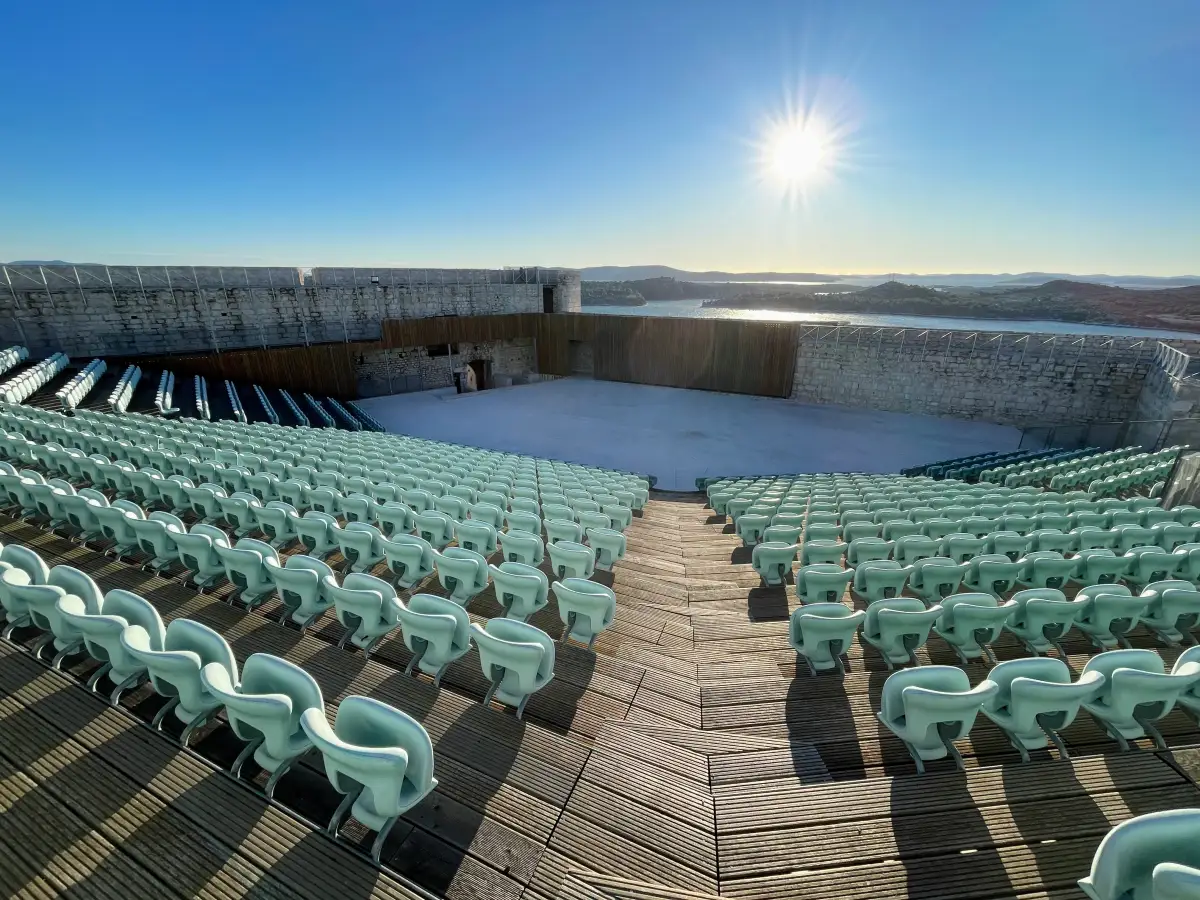 Amphitheater seating and stage at St. Michael's Fortress in Šibenik, with a view of the sea and islands under a bright sun.