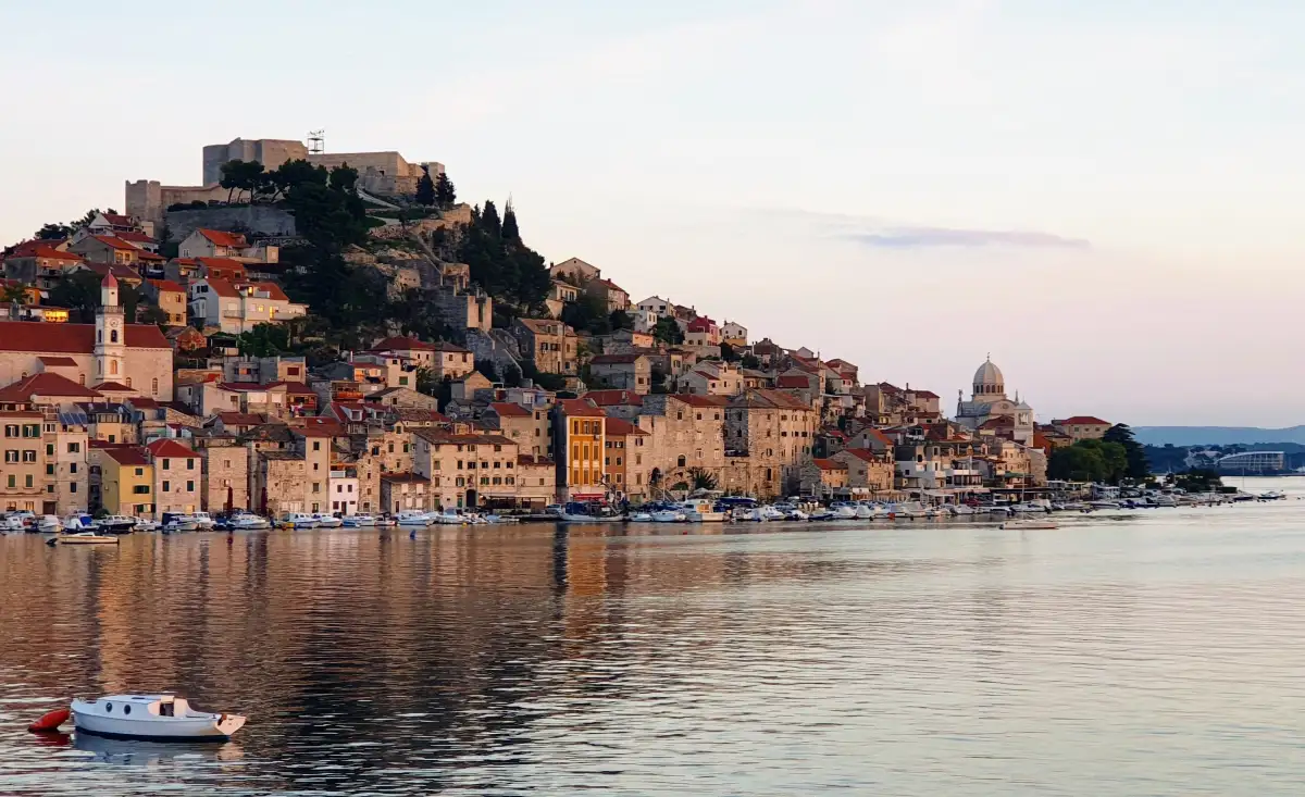 Dusk falls over Šibenik, highlighting its historic architecture and calm marina, with St. Michael's Fortress atop the city.